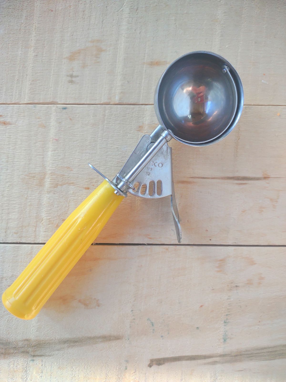 A yellow handled Winco #20 disher on a wood board.