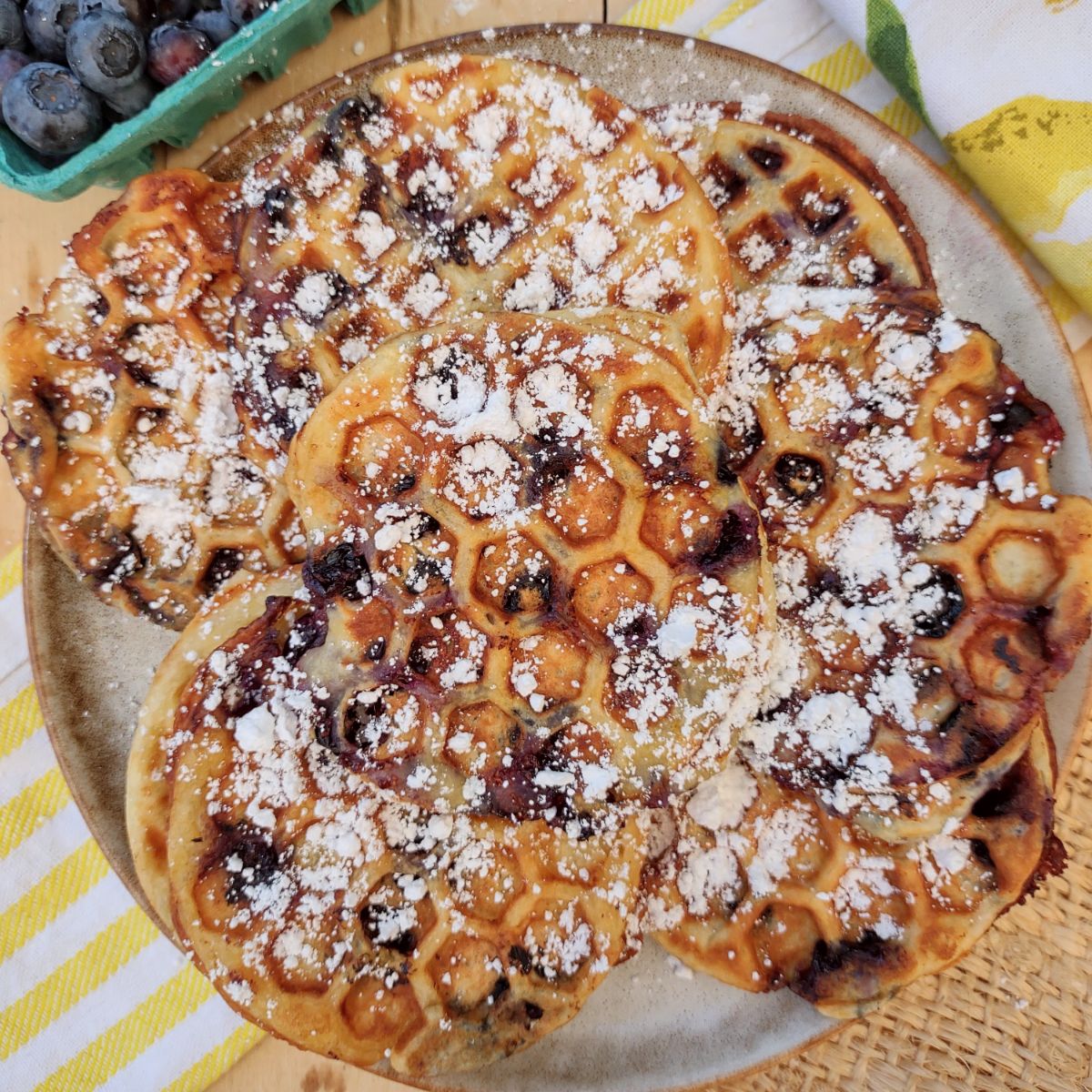 Mini blueberry waffles on a plate topped with powdered sugar.