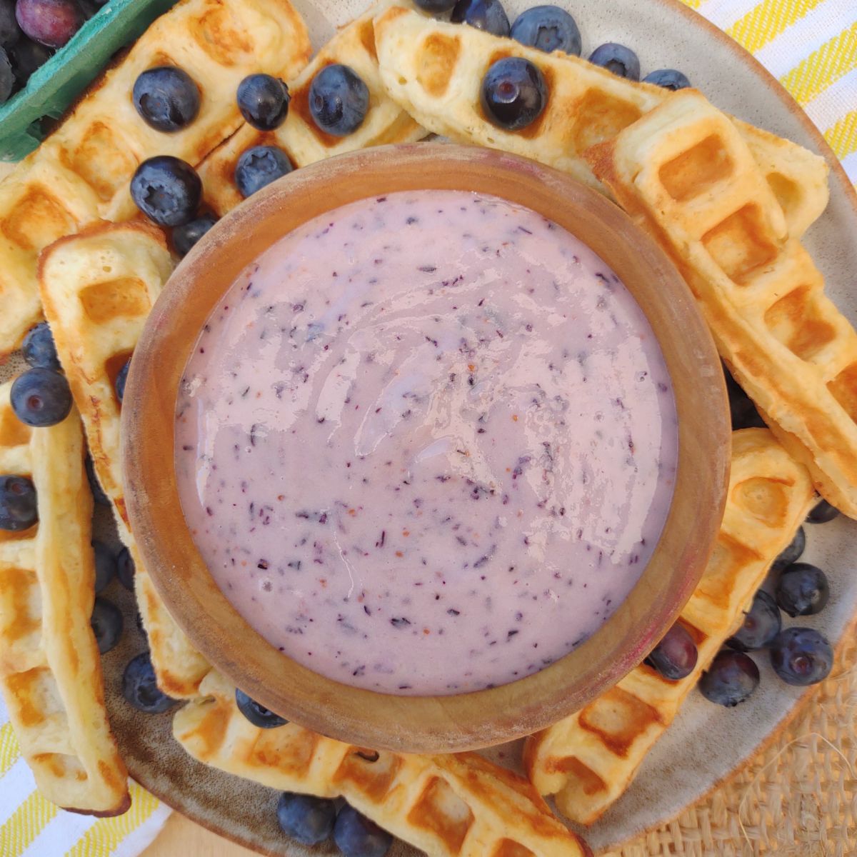 A blueberry dip surrounded by waffle sticks with some whole blueberries on them.