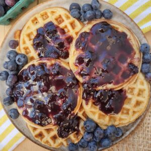 Circle waffles that are glazed with a blueberry brown sugar glaze with fresh blueberries on top.