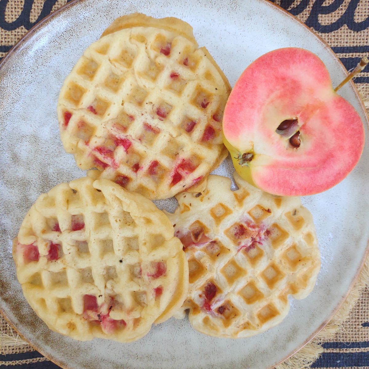 Mini circle waffles that are studded with pink flesh Pink Pearl apples on a gray colored plate.
