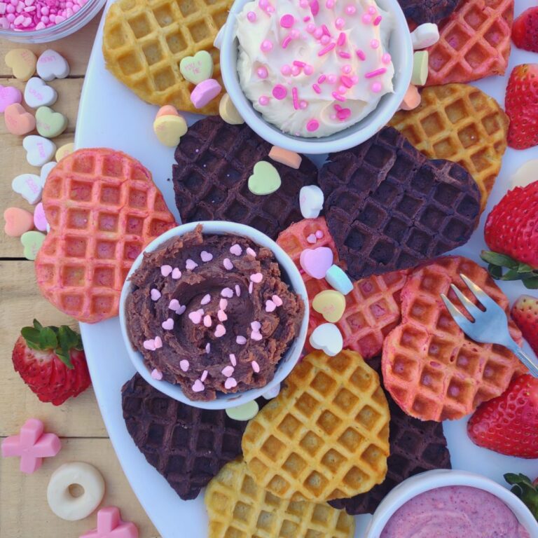 A Valentine's Day themed waffle board with 3 different types of waffles and 3 different types of dips. Conversation hearts and XO gummies adore the platter.